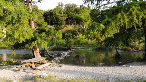 Taking-off-hovering-by-picnic-table-near-recreational-swimming-area-of-the-river-at-sunset