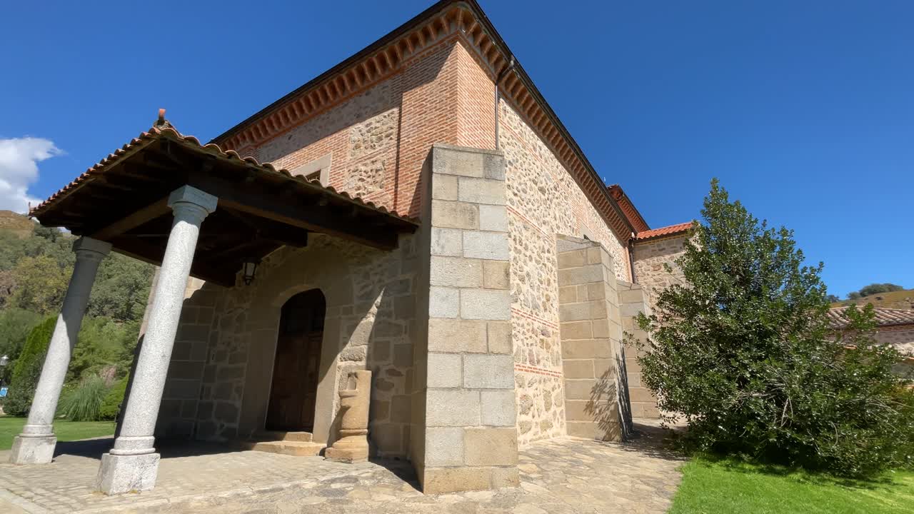 Filming at one of the entrances to a sanctuary we see the wooden portico supported by two round granite columns, with a twist we see its garden area and its surroundings with a blue sky