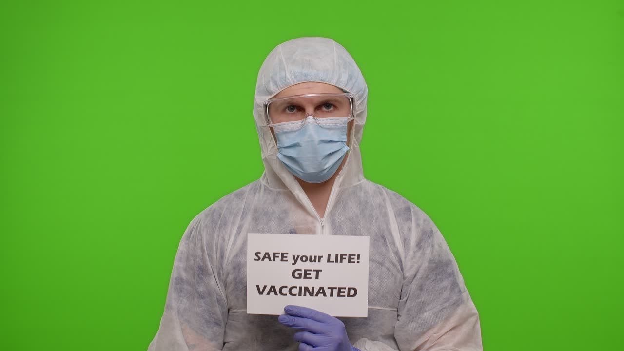 hombre con equipo de protección sostiene un cartel que promueve la vacunación