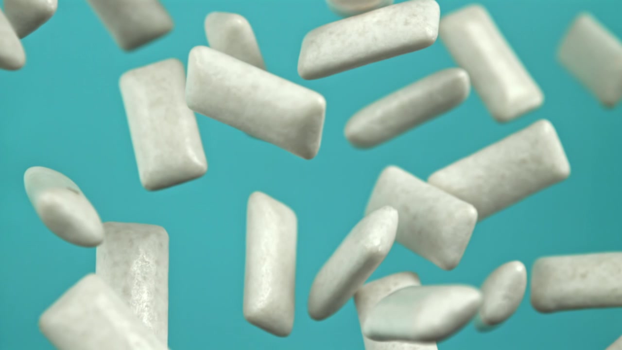 Pezzi di gomma da masticare bianca che cadono al rallentatore su sfondo blu.