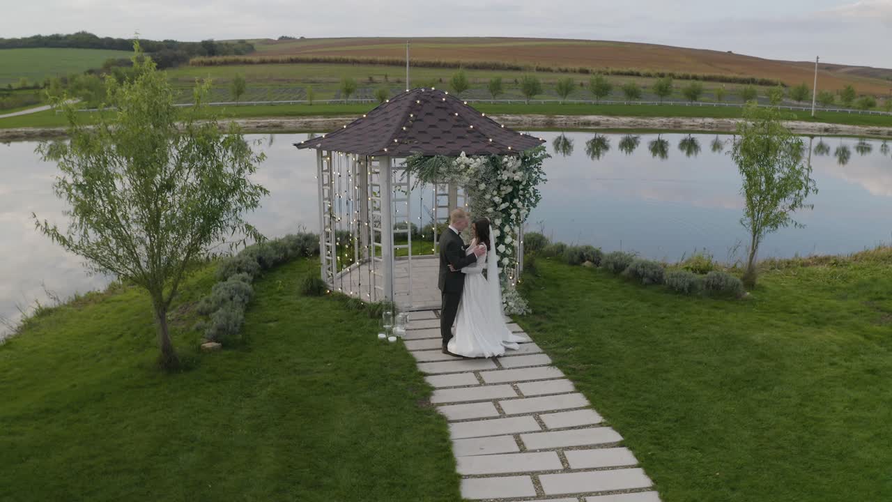 молодожены, жених, невеста обнимаются, обнимаются, целуются, свадьба церемония бракосочетания, арка с цветами