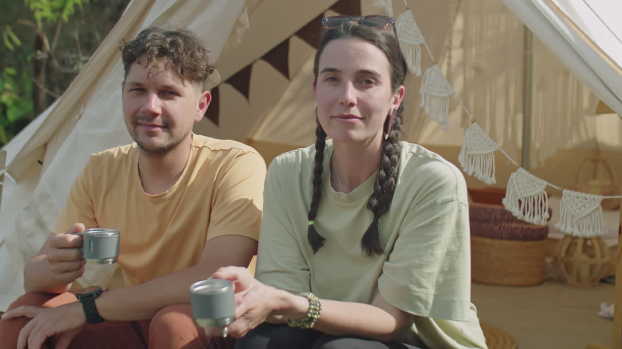Portrait of Young Couple with Tea Mugs Sitting by Glamping Tent