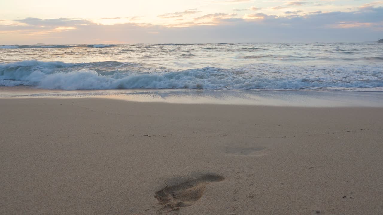 A single footprint is visible in the sand where the waves wash in during a hawaiian sunset on North Shore oahu