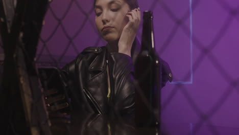 chica seria con chaqueta de cuero bebiendo cerveza y usando el teléfono móvil mientras se sienta en un taburete en la discoteca 1