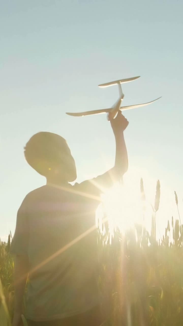 Child playing with toy airplane in a wheat field at sunset