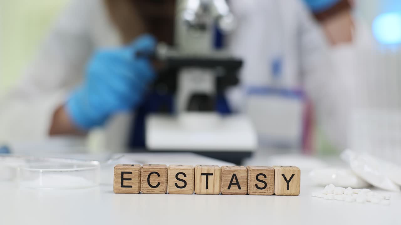 Cubi di legno formano la parola 'ecstasy' vicino a un microscopio e un campione di polvere.