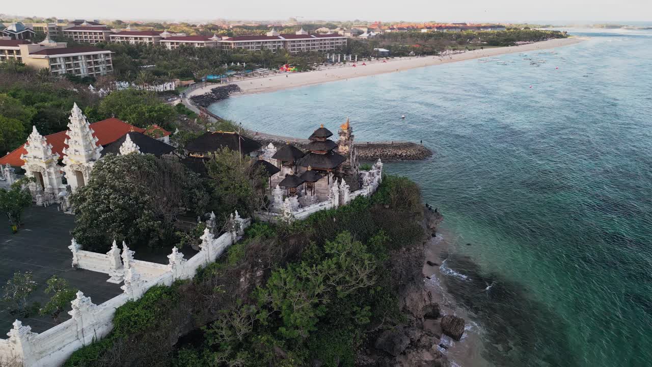 Beautiful drone view of a sacred Balinese seaside temple surrounded by ocean waves and lush greenery, reflecting traditional craftsmanship, serenity, and the timeless harmony of Bali’s coastal spirit