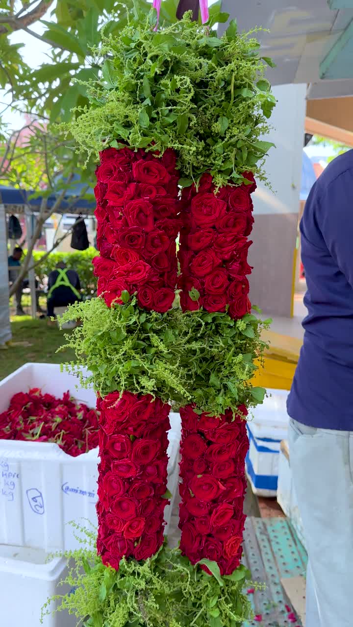 Ghirlanda floreale vivace di rose rosse e basilico sacro che viene calata, di giorno, in un'ambientazione di mercato all'aperto.