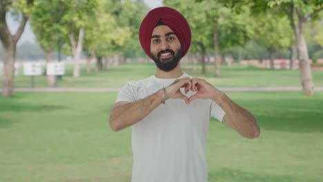 happy sikh indian man showing heart sign in park