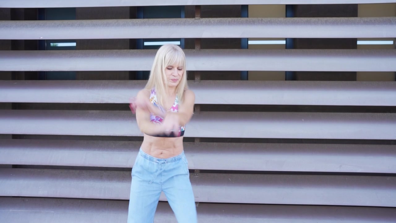 Una giovane donna balla gioiosamente davanti a un edificio moderno, indossando jeans casual e un crop top.