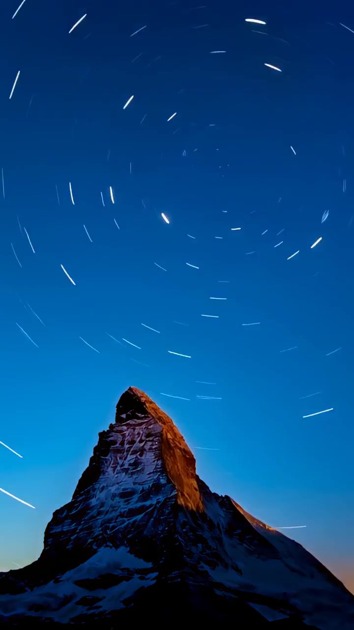 Video verticale: Telecamera che registra e cattura una cima alpina frastagliata mentre il tramonto svanisce, con scie stellari che si formano