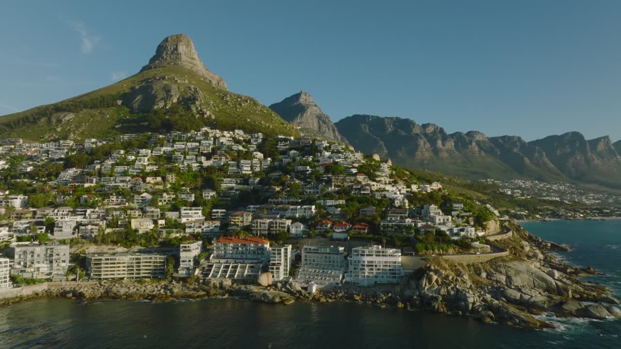 럭셔리 부동산 과 호텔 으로 둘러싸인 해변 을 돌아다니며 비행 한다. 배경 에는 록 마운틴 산맥 이 있다. 케이프 타운, 남아프리카