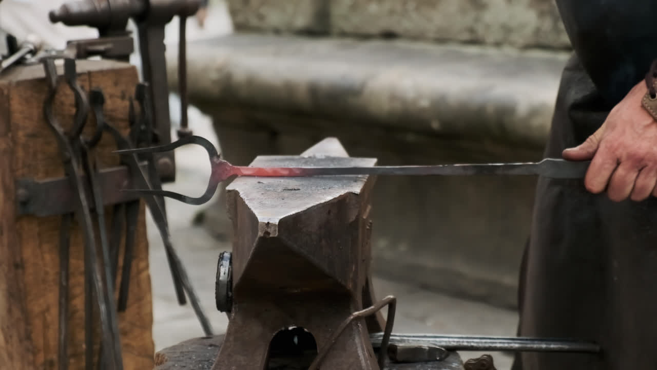 Super slow-motion static shot of a blacksmith finishing a forged piece on the anvil with a hammer; hot metal flakes and sparks burst on impact, tools around the workbench