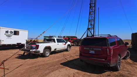 coming closer to cars standing near the truck with oil tower. men work at the equipment for drilling natural resources.