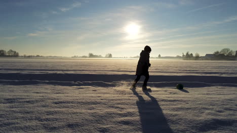 Kleiner-Junge-Spielt-Mit-Einem-Ball-Auf-Einem-Feld-Voller-Schnee