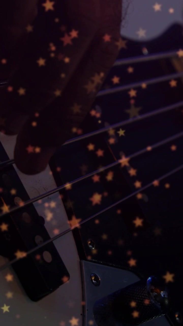 Vertical video: Bass player pressing and plucking strings by pickup, stars moving, playing music