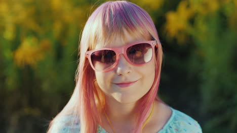 retrato de un niño alegre con gafas de sol rosas y pelo rosa