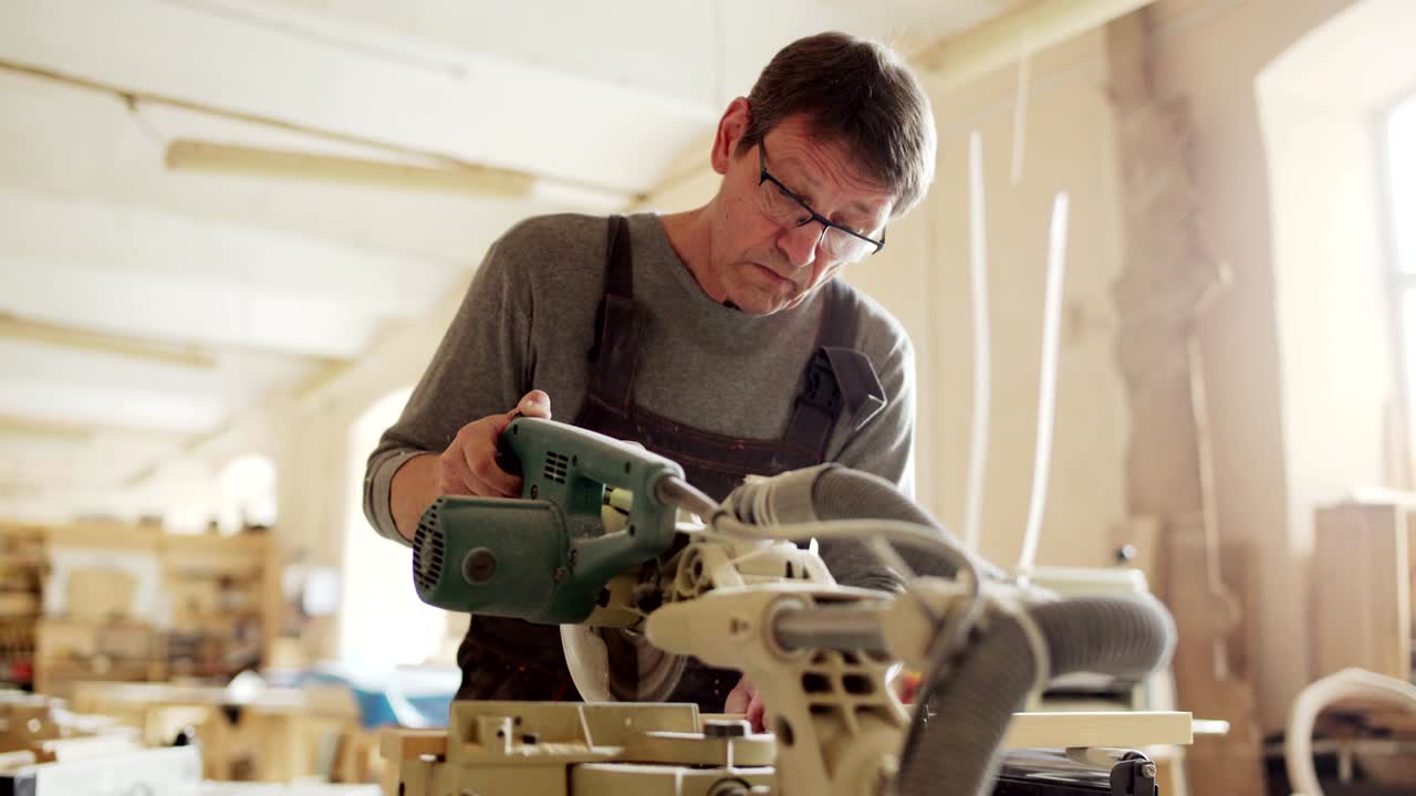 숙련 된 성숙 한 가구 제작자 는 나무판 을 잘라내기 위해 원형 도자기 를 사용 한다