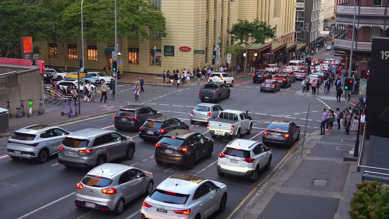 Traffic congestion during peak hours at Edward and Ann streets in Brisbane central business district with pedestrians crossing and cars stoping at traffic light, static shot capturing busy urban life.