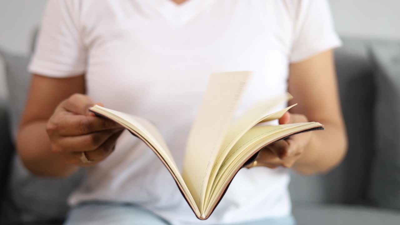 Primo piano di una donna adulta asiatica che legge un libro, mani che voltano la pagina del libro