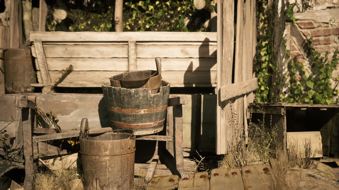 Vecchio capanno in legno con secchi rustici e una recinzione rovinata dal tempo alla luce del sole.