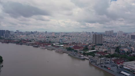 aerial shot along saigon river port with navy ships, tourist boats and urban sprawl