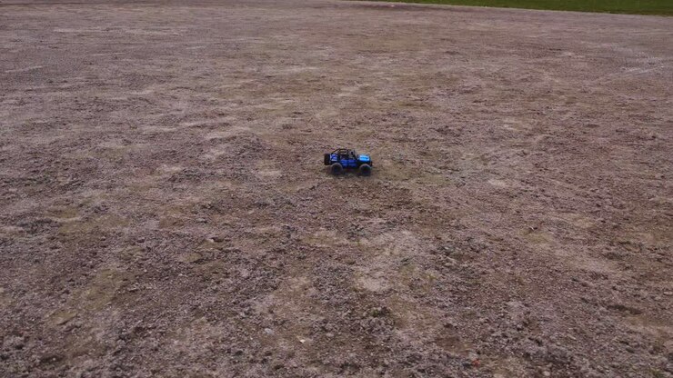 A miniature electric 4WD vehicle races over a rough terrain, leading the way for an outdoor competition