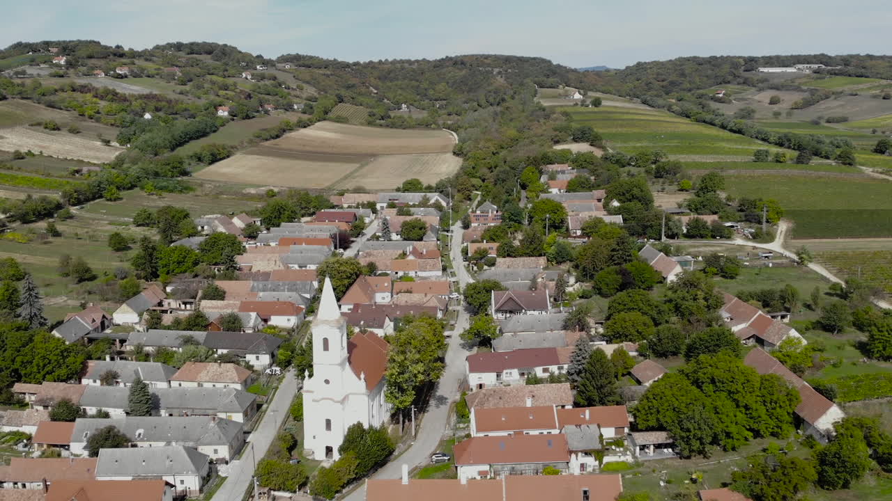 sobrevolando un pequeño pueblo, con una iglesia católica, tierras agrícolas alrededor y un bosque