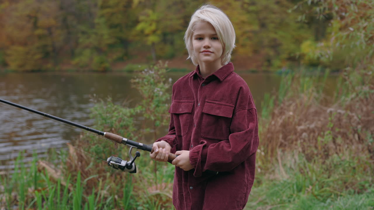 A young blonde boy holding a fishing rod by a lake in nature