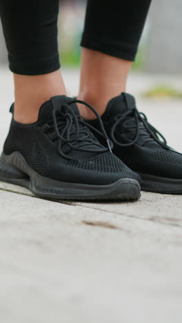Close-up view of runners leg in black sneakers, stretching out ready to move, on a smooth paved path with blurred natural background, preparing for a run or jog