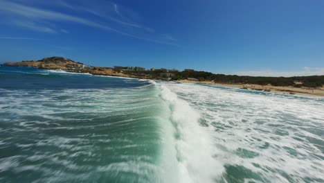 Fpv-Drone-Volando-Cerca-De-Surf-Y-Rompiendo-Olas-En-Un-Hermoso-Día-De-Playa-Con-Agua-Azul-Clara-Y-Cielos