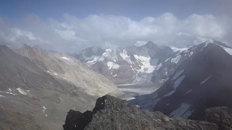 Aerial-discovering-shot-of-a-valley-in-the-swiss-alps-and-an-edged-peak-in-a-summer-day-with-clouds