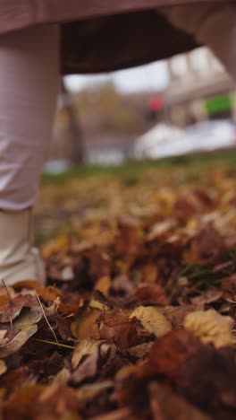 woman walking through autumn leaves in city park