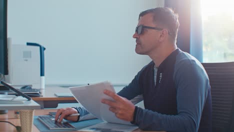 busy european dutch caucasian white man male adult model with glasses working in the office job on desktop workspace with paper documents and pc, digital film look