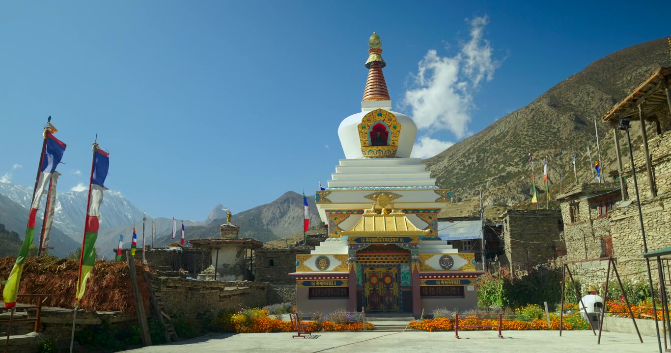 Annapurna Circuit, Manang Nepal, Traditionelt hvidt og guld buddhistisk chorten-monument med bedeflag, nær Himalaya-bjergtoppene under en klar blå himmel.