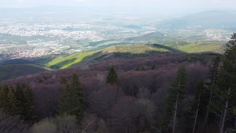 Clip-Cinematográfico-De-Drones-Sobre-Los-Frondosos-Bosques-En-Las-Montañas-De-Vitosha-Con-Una-Ciudad-En-El-Valle