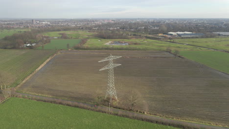 Jib-down-of-large-electricity-transmission-towers-in-countryside-with-a-city-in-the-background