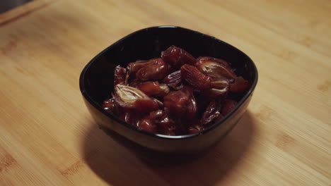 Woman-hand-puts-a-grasp-of-date-fruits-into-a-small-black-bowl