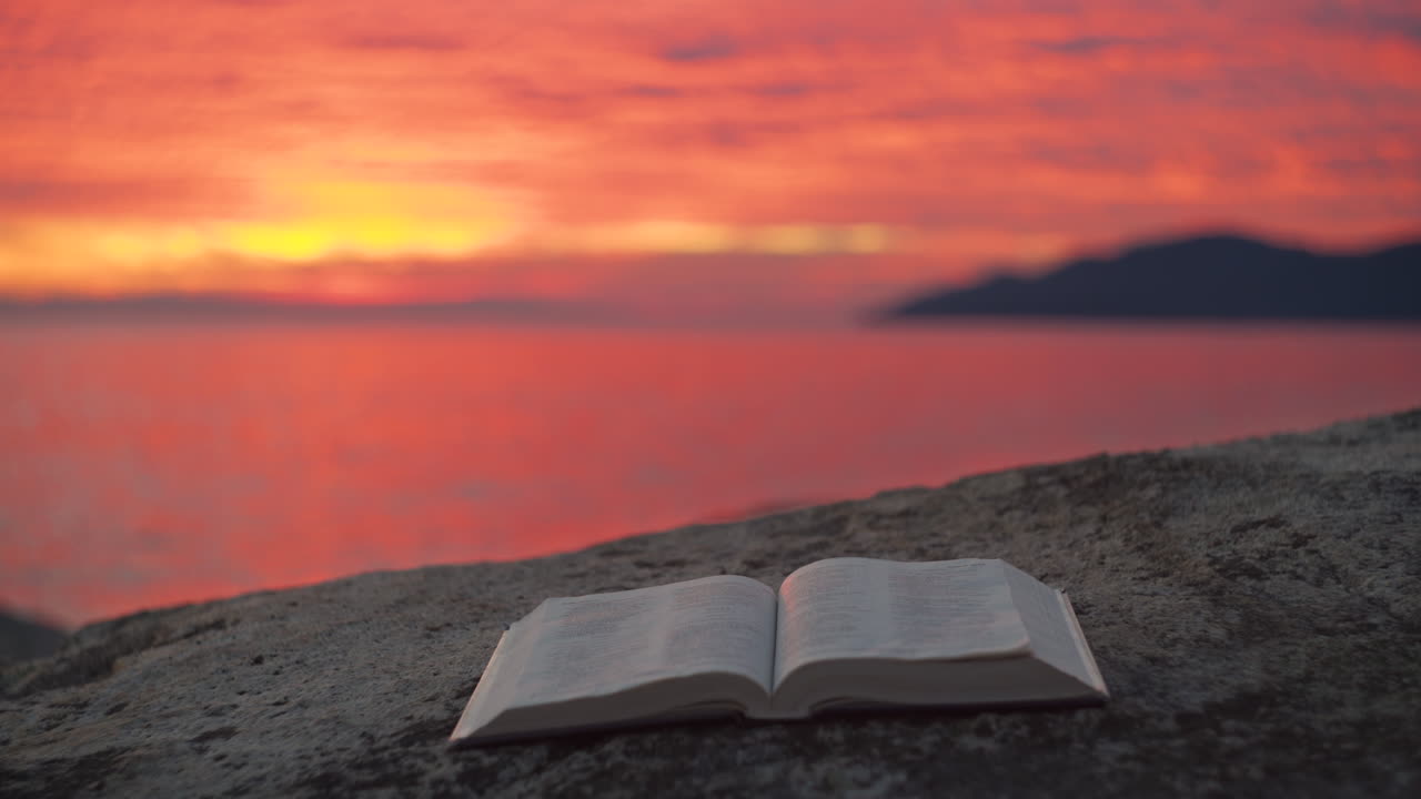 A Bible Resting in the Foreground of a Brilliant and Colorful Sunset