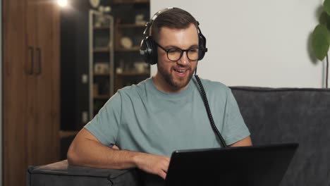 handsome man in glasses puts on headphones and waves hello to laptop webcam