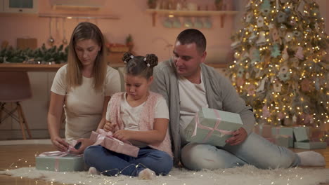 mother, father and little girl opening christmas presents