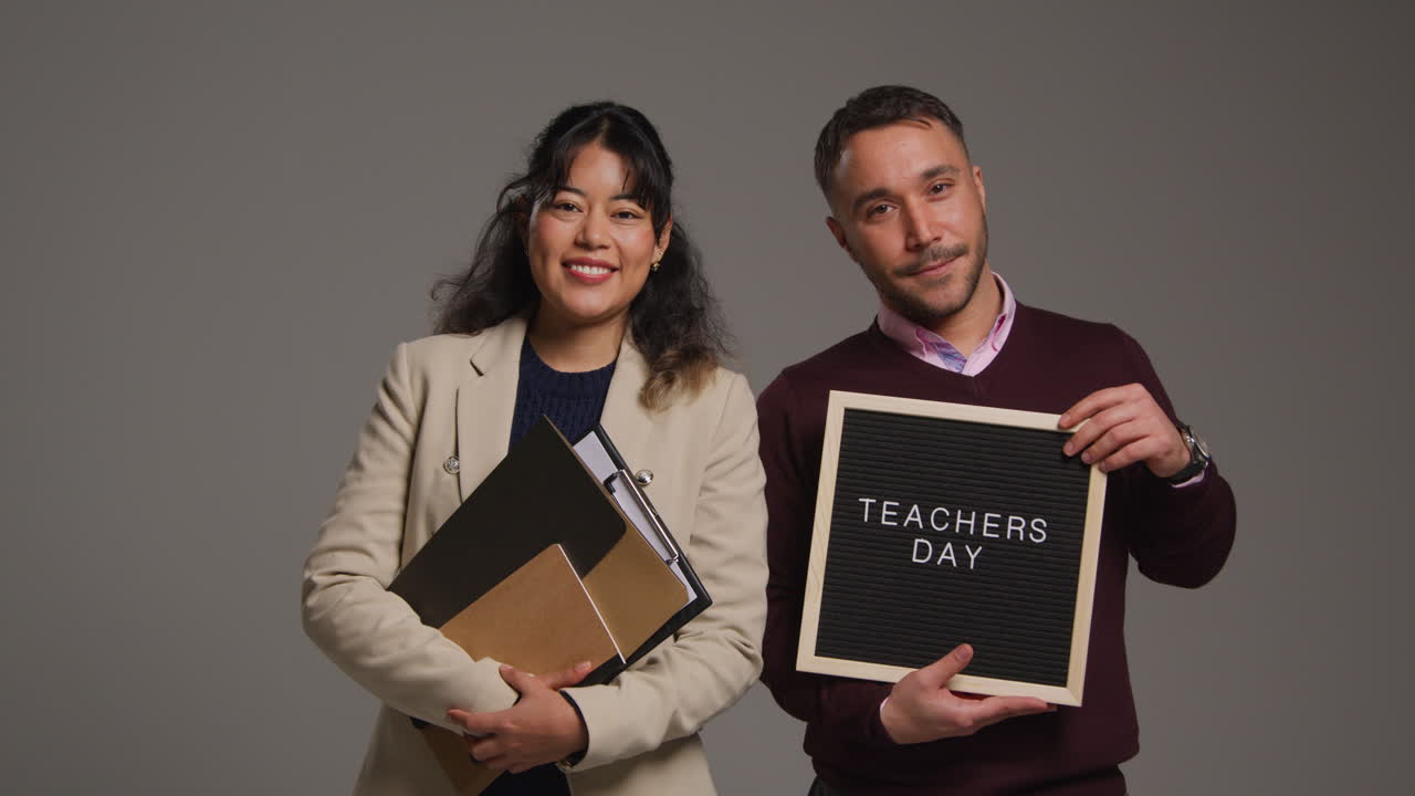 retrato de estudio de maestros y maestras sonrientes sosteniendo un tablón de anuncios leyendo el día de los maestros contra un fondo gris