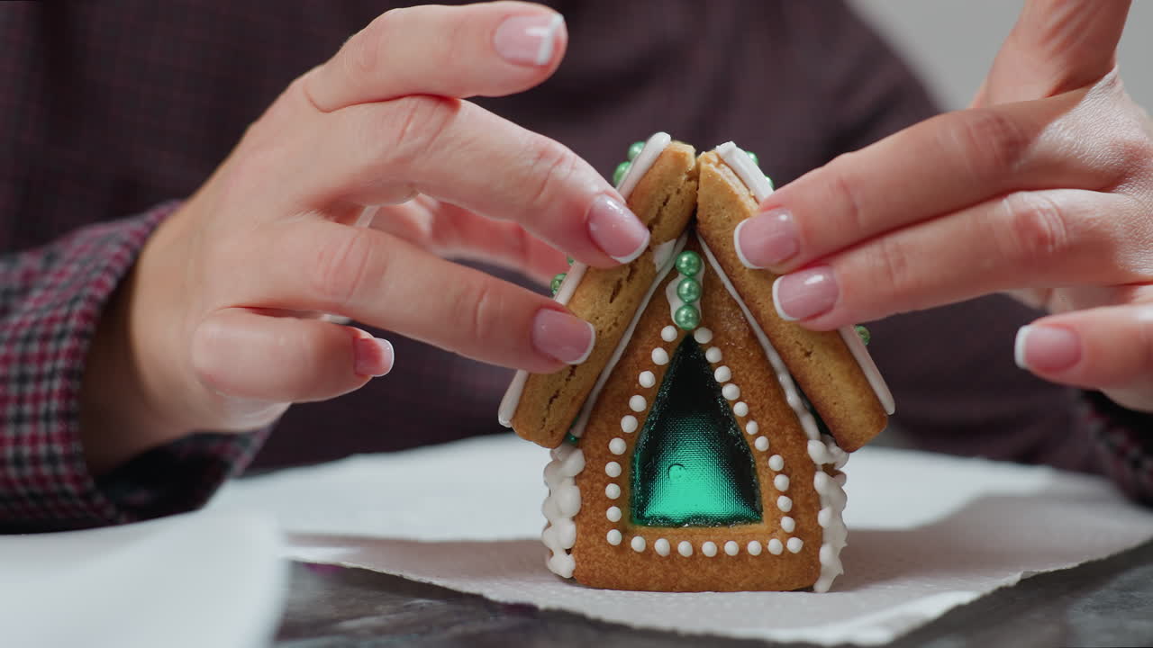 primer plano de un panadero estabilizando una galleta de pan de jengibre recién ensamblada con un hielo delicado y decoraciones intrincadas, sosteniendo cuidadosamente la estructura para asegurarse de que se ajuste correctamente en una servilleta blanca
