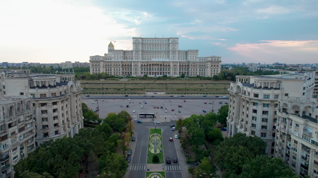 vista aérea del palacio del parlamento en bucarest, rumania con un cielo azul claro en el fondo al atardecer, vegetación exuberante y fuentes de agua debajo, movimiento lento hacia adelante