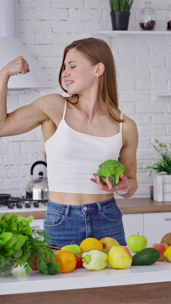 Fit smiling woman in kitchen. Young woman with muscular body standing in the kitchen. Vertical video