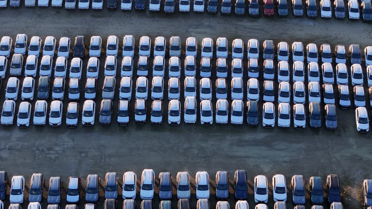 Dronebillede i fugleperspektiv viser importerede biler parkeret i parallelle rækker på en lagerplads, der fremhæver håndtering af køretøjer i stor skala