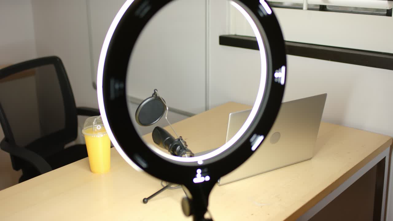 Ring light is starting rotation on tripod, shifting circle, revealing cup, mic, laptop on desk