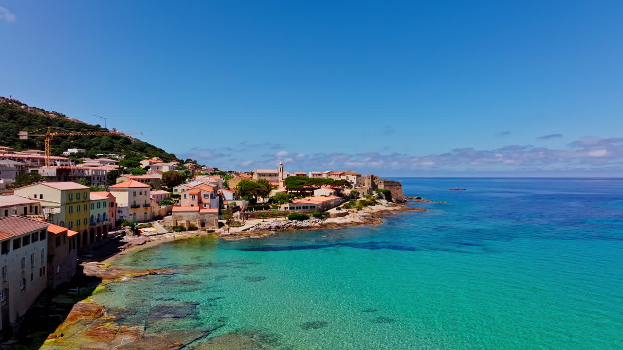 Aerial drone shot over the coastal town of Algajola in Balagne, Corsica, France. High view of the local town and the turquoise sea. Bright blue sky. Summer holidays destination