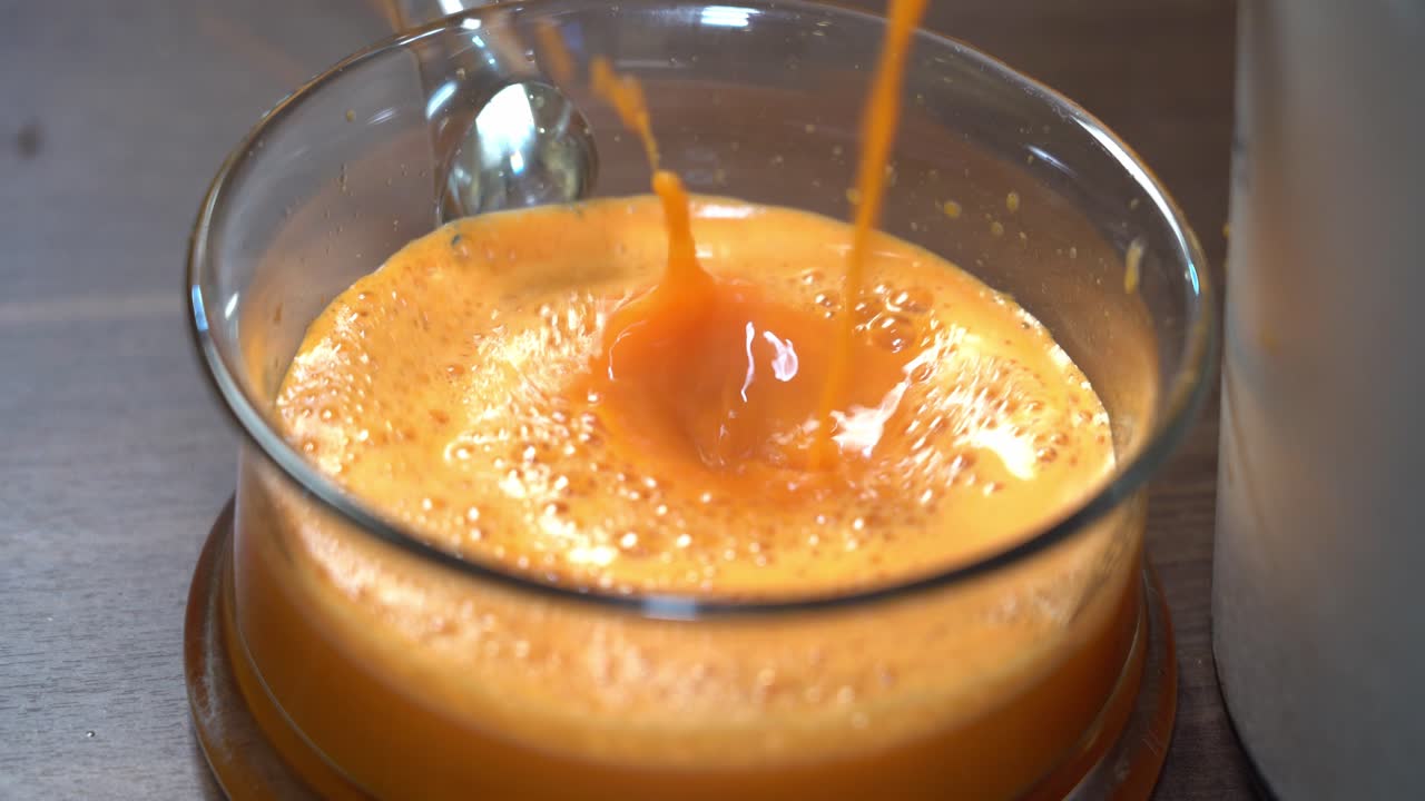 Succo fresco di arancia e carota che si riversa dall'estrattore in una ciotola di vetro, con schizzi e schiuma naturale