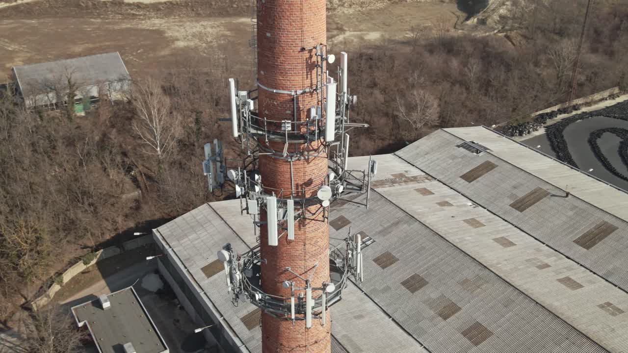 Flying around of an old industrial brick chimney equipped with multiple telecommunications antennas.